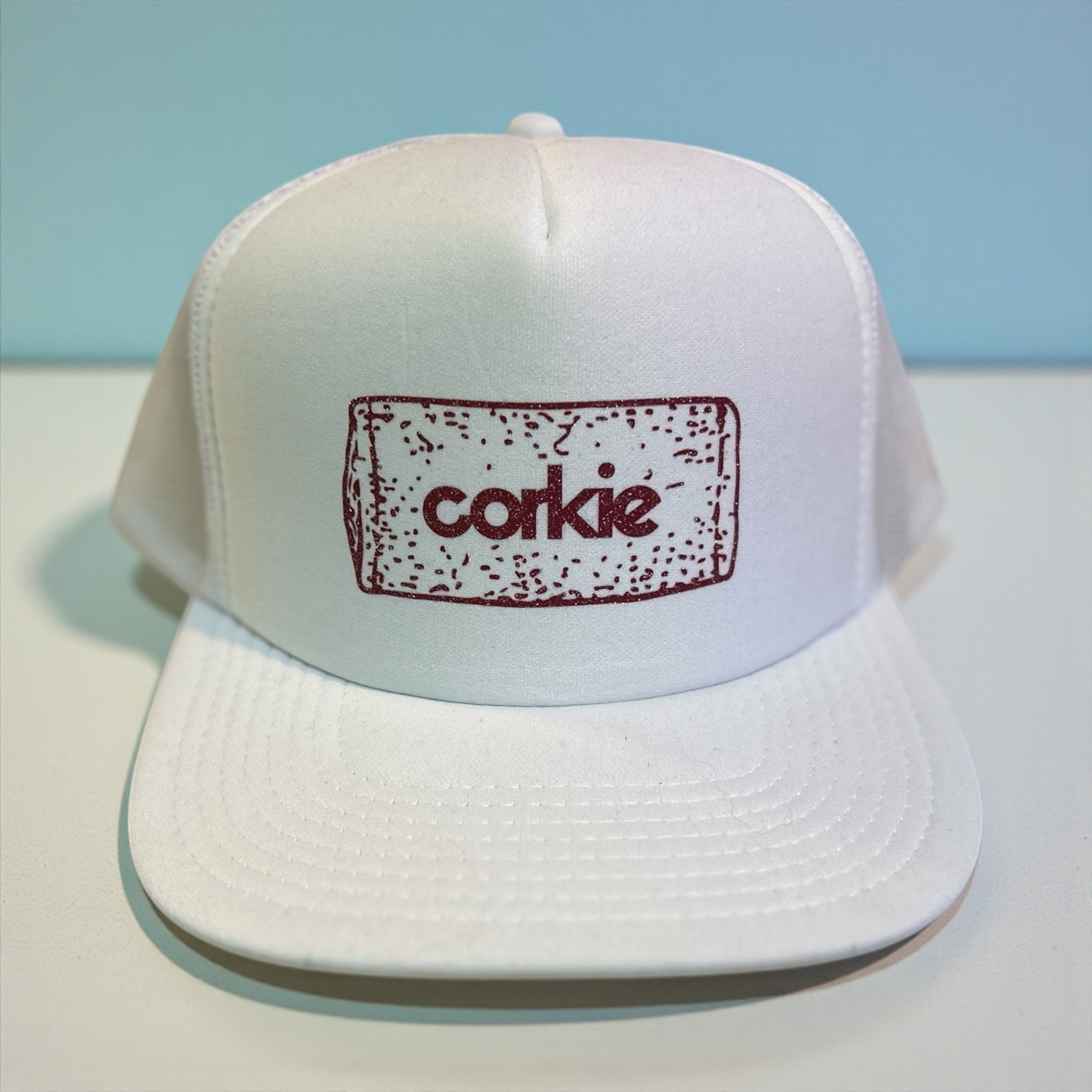 White cap with 'corkie' logo on a light blue background