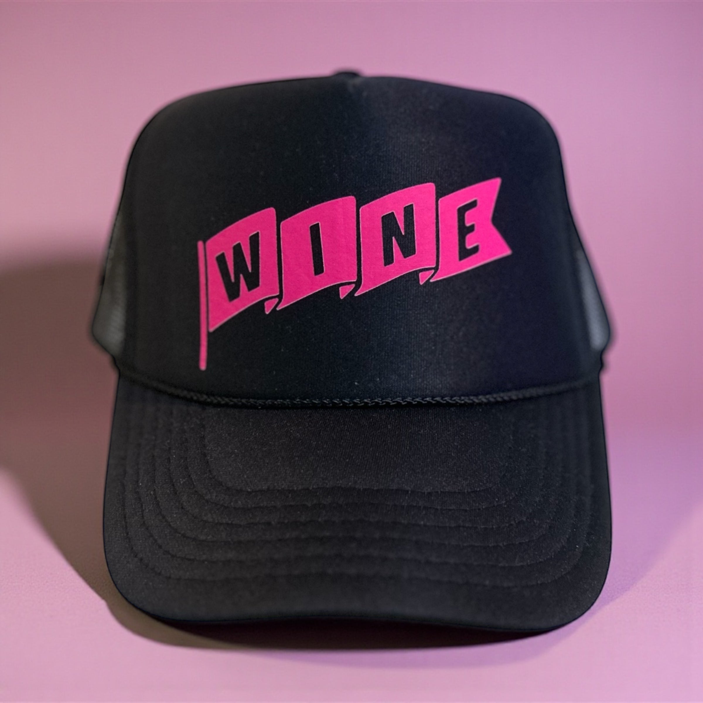 Black corkie foam trucker cap with pink 'WINE' text on a pink background